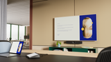 A photograph of a meeting space. At the front of the room, against the wall, there is a TV screen with a Logitech MeetUp 2 mounted below the display. In front of the screen, there is a table with a Logitech Tap IP and laptop on it. The laptop is connected to the MeetUp 2 via a cable for BYOD mode.