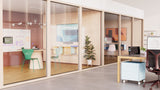 A photo taken from an open plan office space, facing two meeting rooms. In both meeting rooms, underneath the TVs, are visible Logitech Rally Bar Huddle cameras.