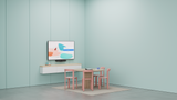 A photo of a meeting room set up for Google Meet. On the far wall is a TV underneath which is the Logitech Rally Bar Huddle. In front of the TV is a round table with four pink chairs.