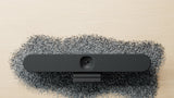 A front-facing image of the Logitech Rally Bar Huddle lying in what appears to be plastic pellets, a reminder that this camera is produced using post-consumer recycled plastics.