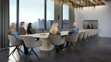 An image of a large boardroom. Six people are sitting at the far end of a long 20-seat table with the Neat Pad placed on the table between them. At the other end is the Neat Board Pro mounted on the wall. On the screen is a woman smiling, appearing to be on a live video call.